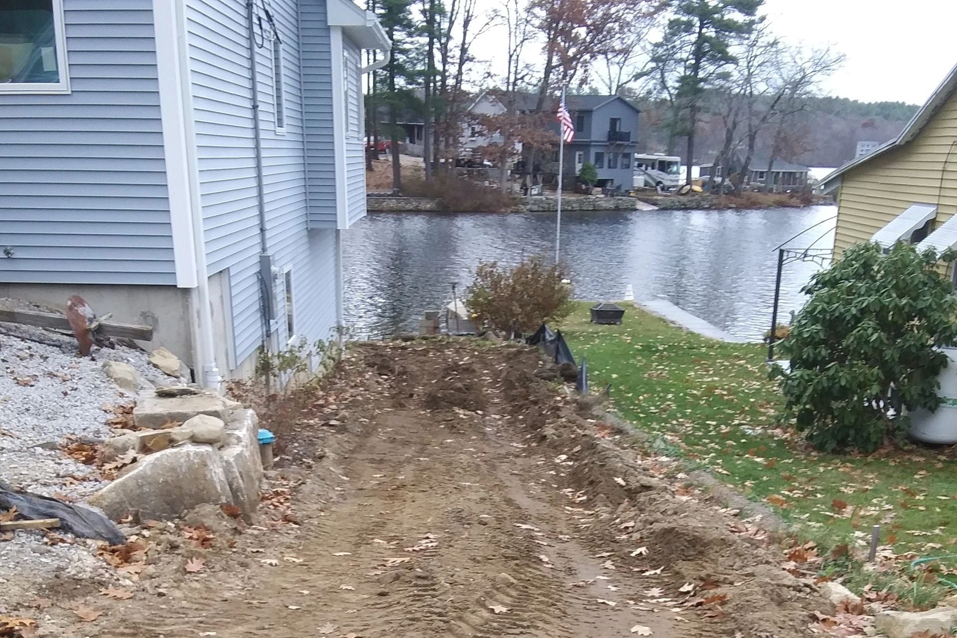 Muddy dirt path running between a lake house and the water, with scattered leaves and uneven terrain. Project by KRD Landscaping in Charlton.