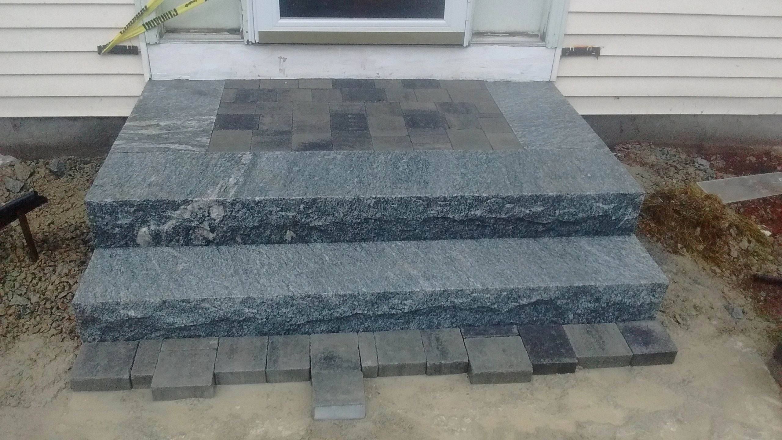 Newly installed granite steps and a paver landing in Webster, MA, in front of a house entrance, with caution tape indicating ongoing construction. Project by KRD Landscaping.