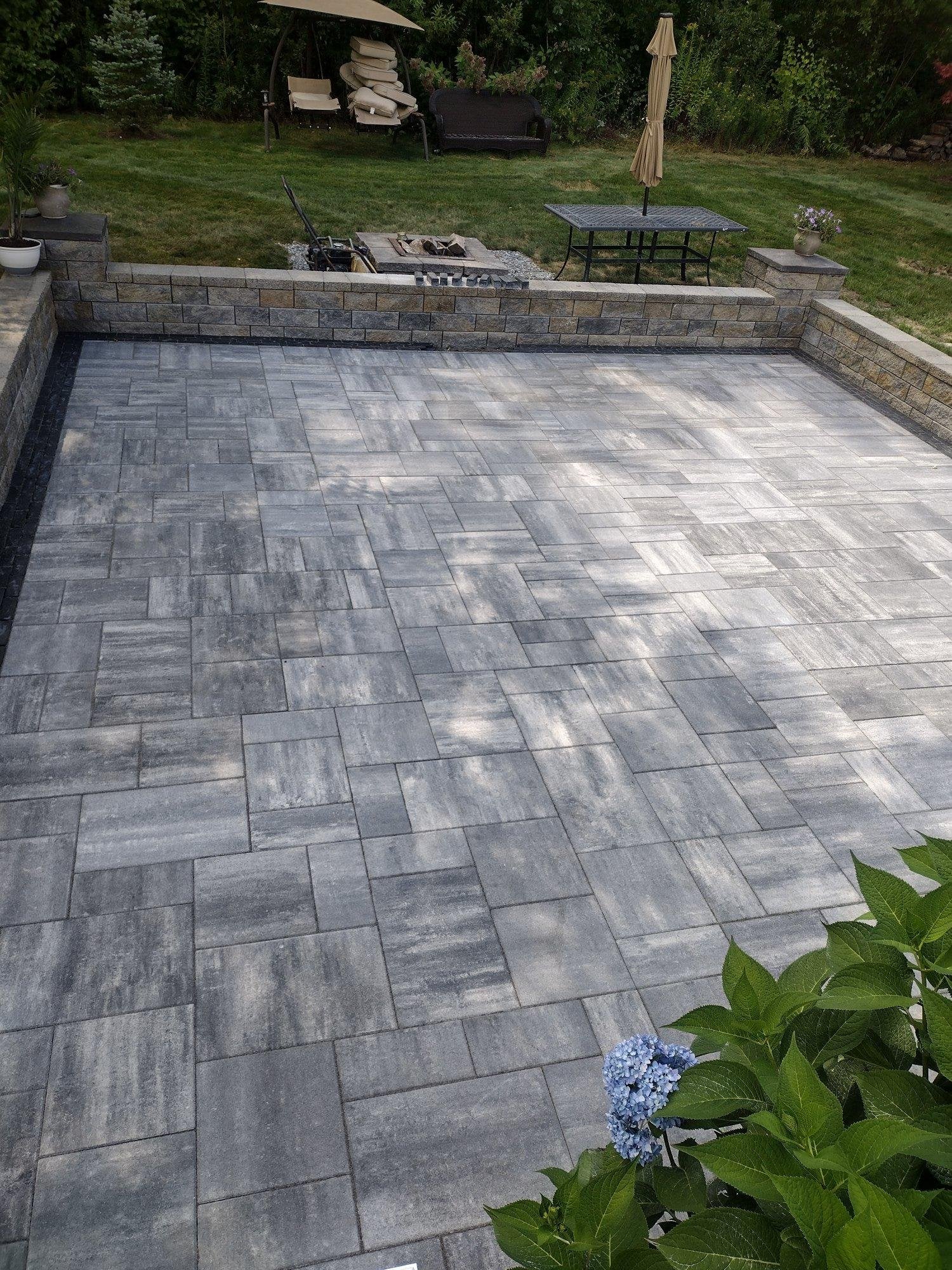 Crushed stone gravel base being spread and compacted for large format paver patio installation with block wall footings in Luster, MA by KRD Landscaping.