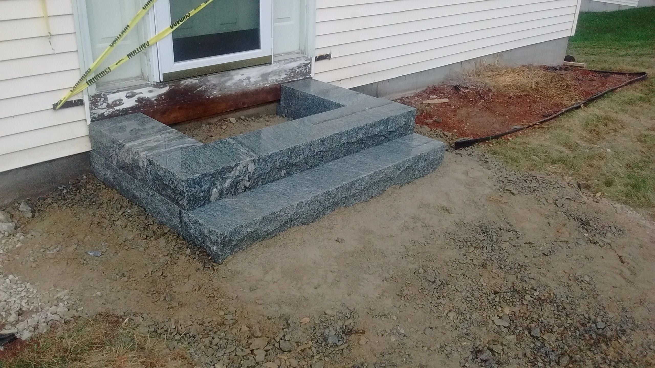 Partially constructed granite steps in Webster, MA, surrounded by gravel, dirt, and caution tape, showcasing the progress of the entry renovation. Project by KRD Landscaping.