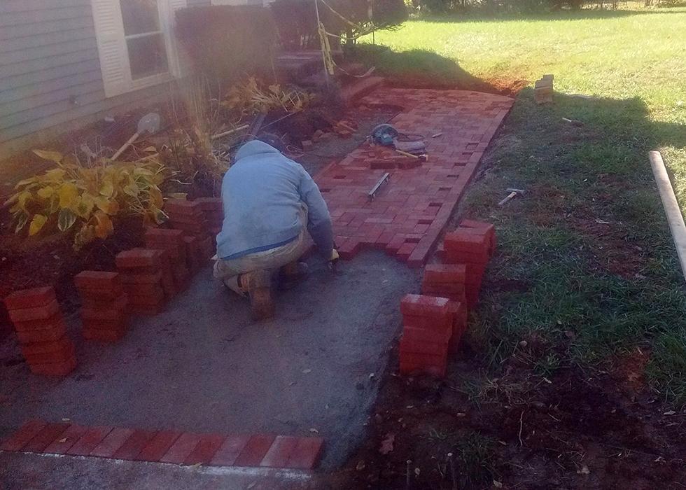 KRD Landscaping hardscape installer laying brick pavers for a walkway at a Central Massachusetts home — join our landscaping crew
